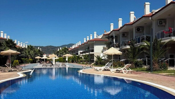 A swimming pool with lounge chairs and umbrellas, surrounded by hotel buildings with red-tiled roofs. - Beautiful 2-bedroom condo with AC in enchanting in Sunset Beach Club,Fethiye (Muğla)