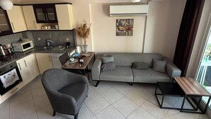 A modern living space with a kitchen, a gray sofa, a small table, and a ceiling fan. - Beautiful 2-bedroom condo with AC in enchanting in Sunset Beach Club,Fethiye (Muğla)