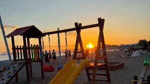 A beach playground with a yellow slide and swings, set against a sunset. - Beautiful 2-bedroom condo with AC in enchanting in Sunset Beach Club,Fethiye (Muğla)