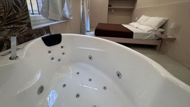 A modern bathroom with a freestanding bathtub, a shower area, and a bed with a headboard.