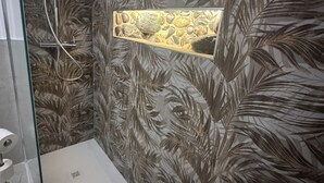 A shower with a glass door, a wall with a leaf pattern, and a rectangular stone accent.
