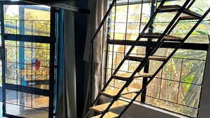Une pièce avec un lit, un escalier, une fenêtre et un petit tabouret.