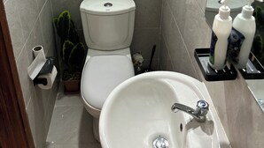 Une salle de bain équipée de toilettes, d’un lavabo et de deux flacons de gel hydroalcoolique placés sur un plateau.