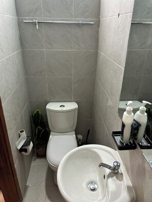 Une salle de bain équipée de toilettes, d’un lavabo et de deux flacons de gel hydroalcoolique placés sur un plateau.