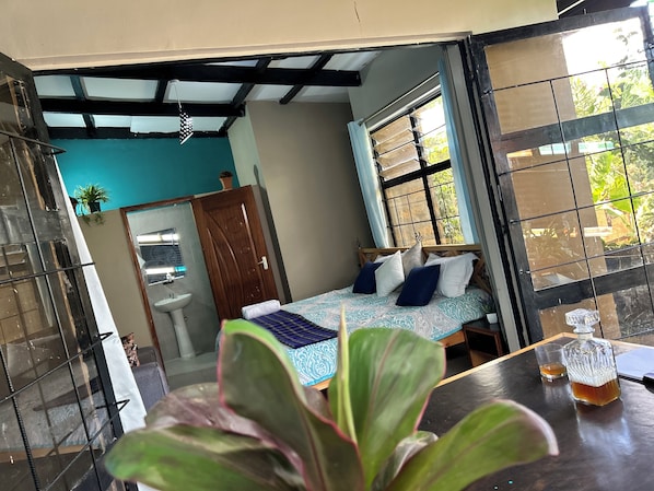 A bedroom with a bed, a window, a sink, and a potted plant.