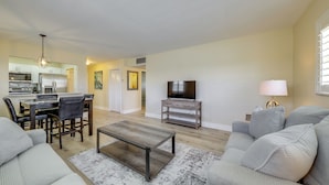 A living room with a sofa, coffee table, TV, and a dining area with chairs and a table. - Walk to Beach, Steps to Pool, Beach Chairs (Pompano Beach)