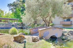 Un puente sobre un estanque, rodeado de rocas y vegetación, con un edificio al fondo.