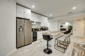 A modern kitchen with a stainless steel refrigerator, white cabinets, a granite countertop, and a bar area with bar stools. - Explore The Springs! Family-friendly Basement Unit (Colorado Springs)