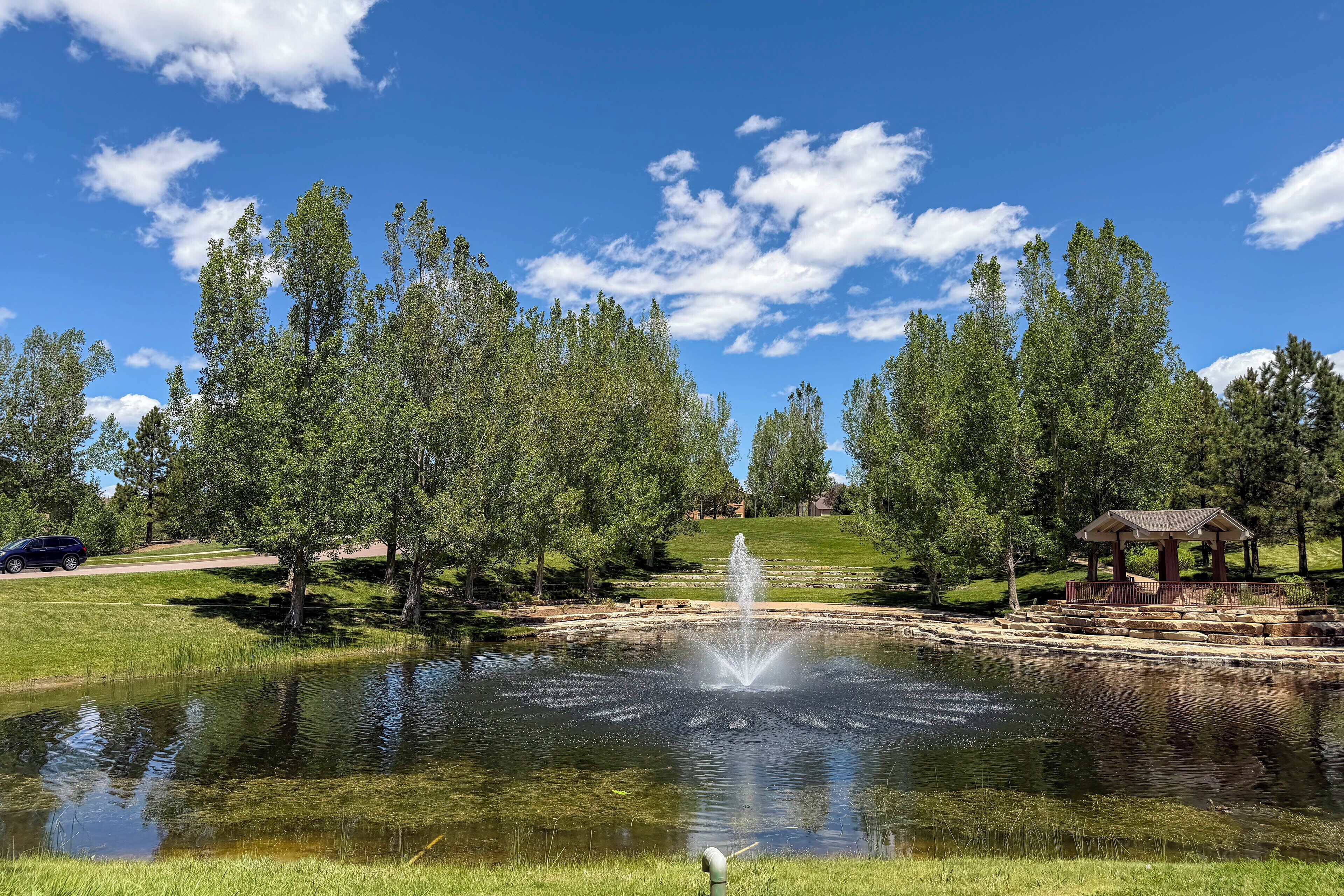 Un étang avec une fontaine, entouré d’arbres et agrémenté d’un kiosque.
