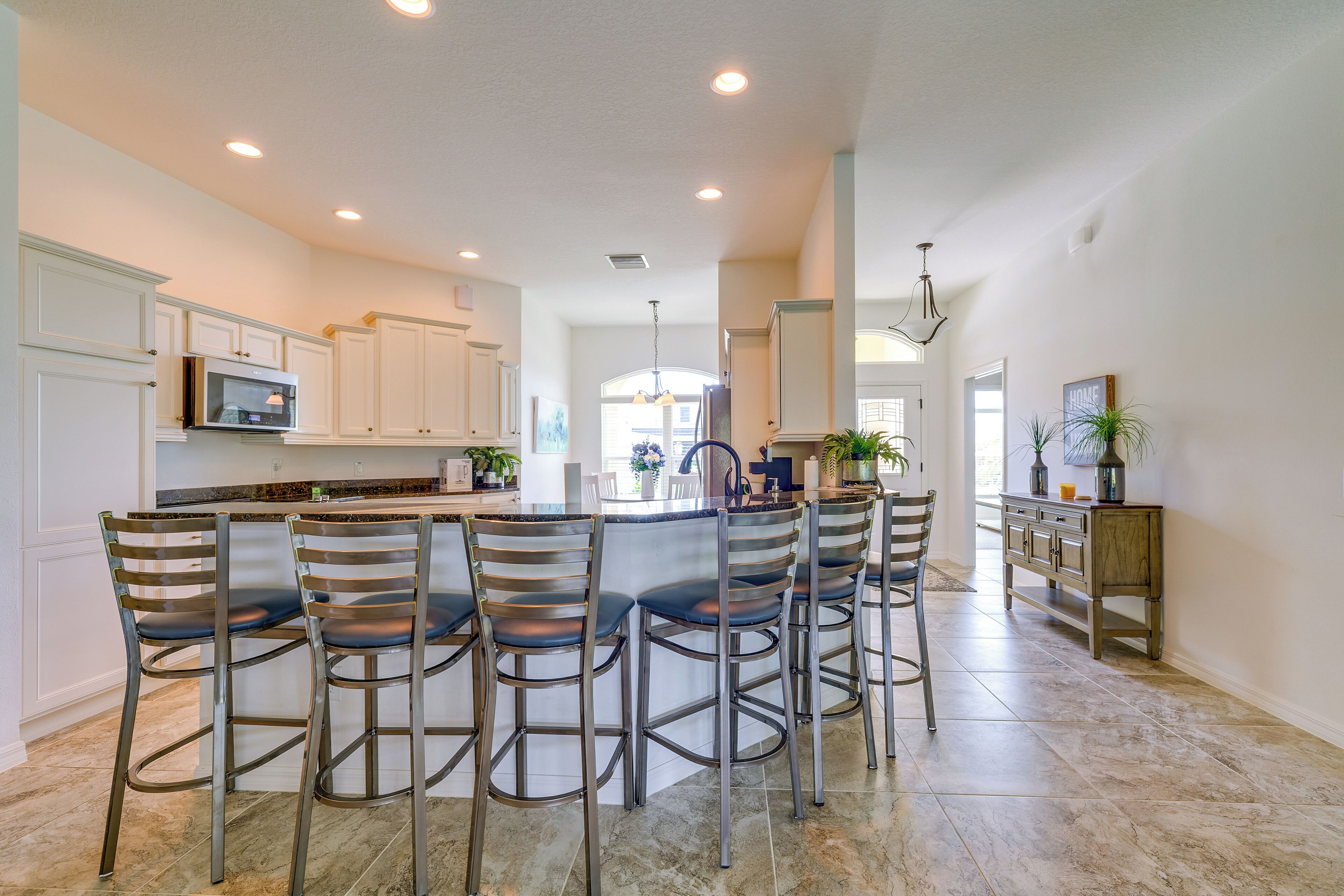 A modern kitchen with white cabinets, a central island with bar stools, and a dining area with a chandelier.