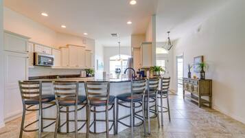 A modern kitchen with white cabinets, a central island with bar stools, and a dining area with a chandelier.