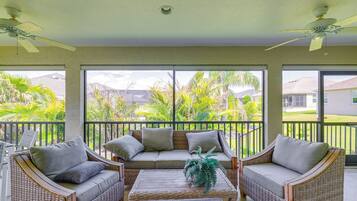A covered patio with wicker furniture, large windows, and ceiling fans.
