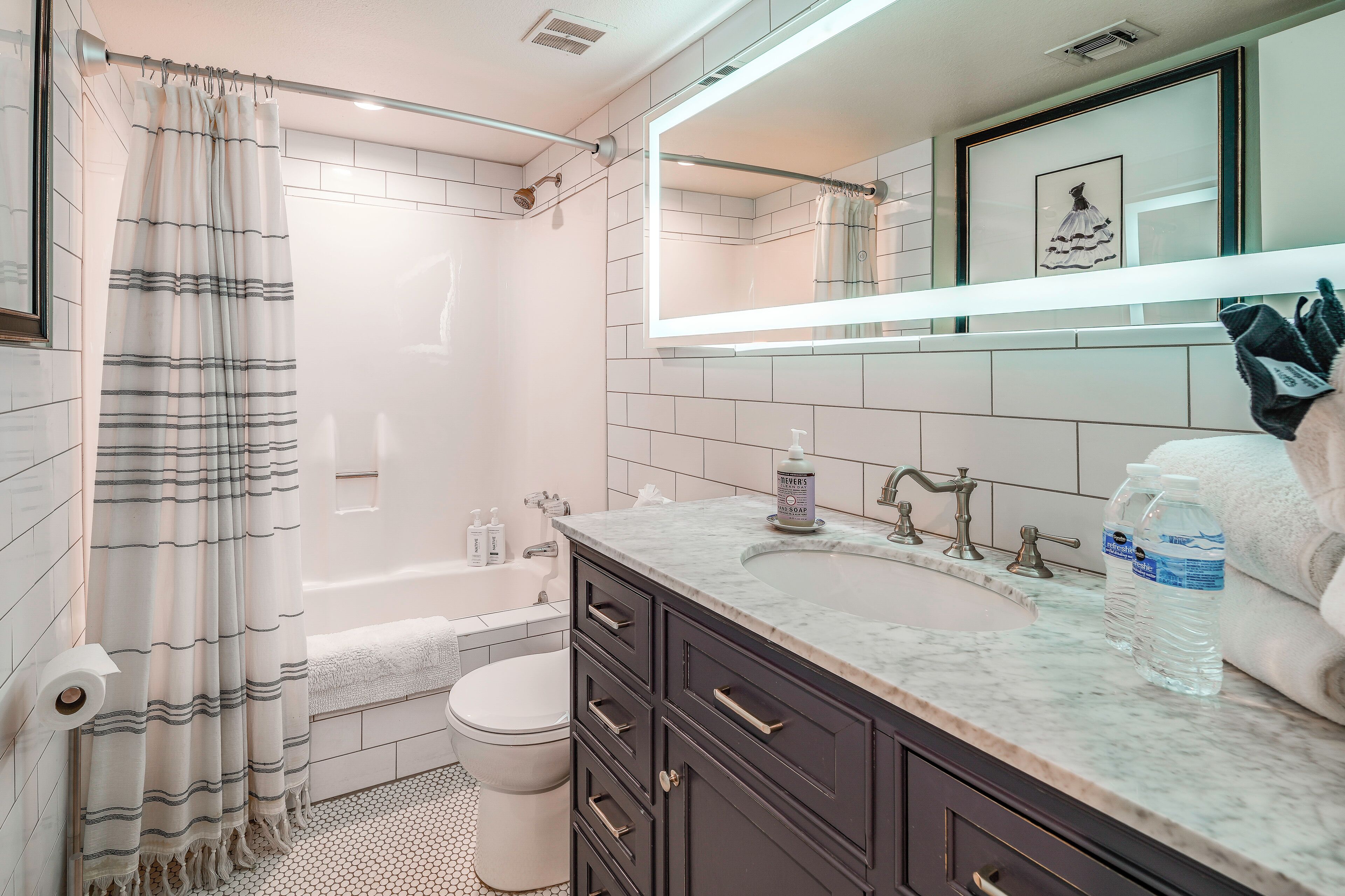 A bathroom with a bathtub, toilet, vanity with a sink, and a mirror.