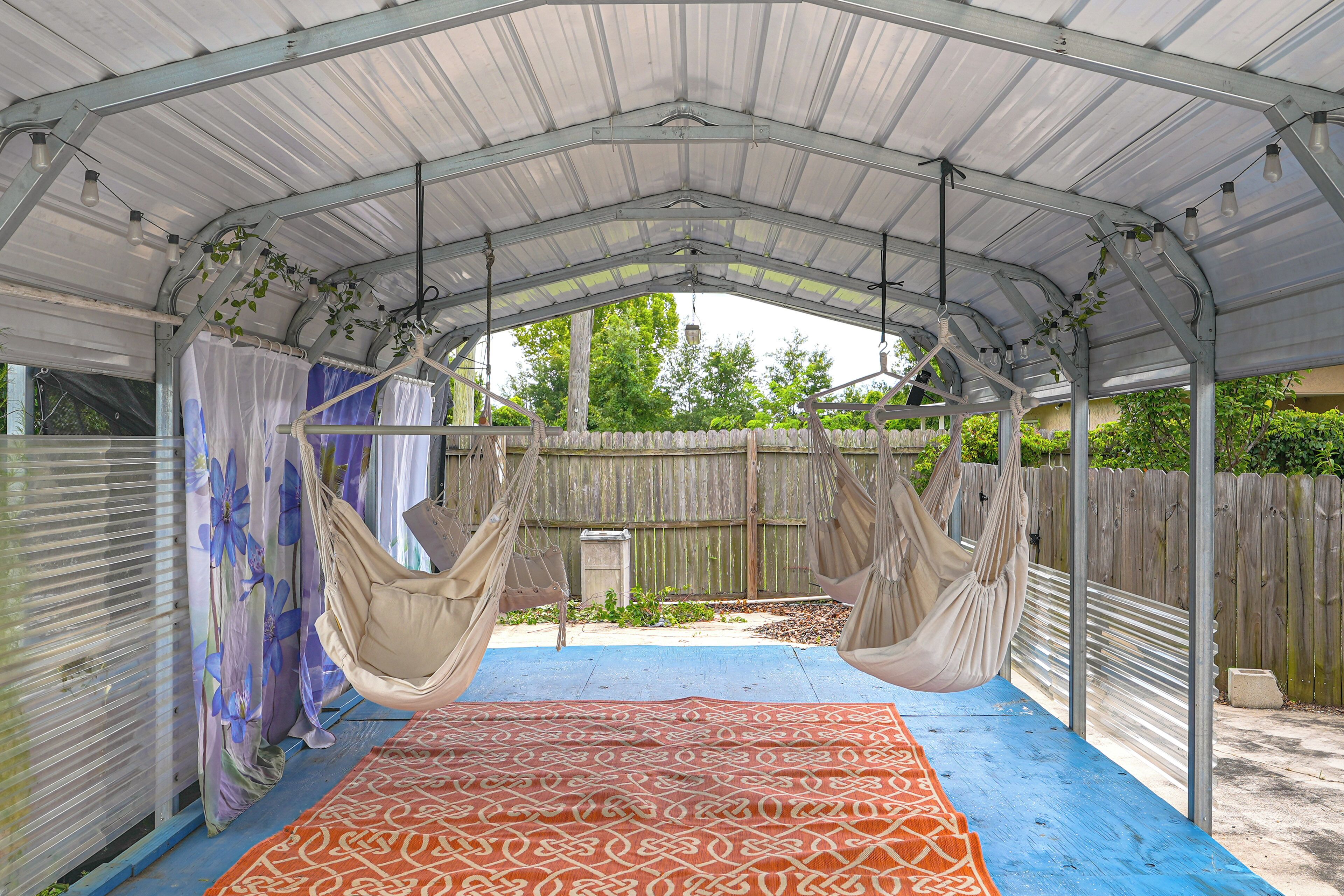 Un espacio de patio cubierto con una hamaca, un tapete estampado y vistas al jardín trasero.