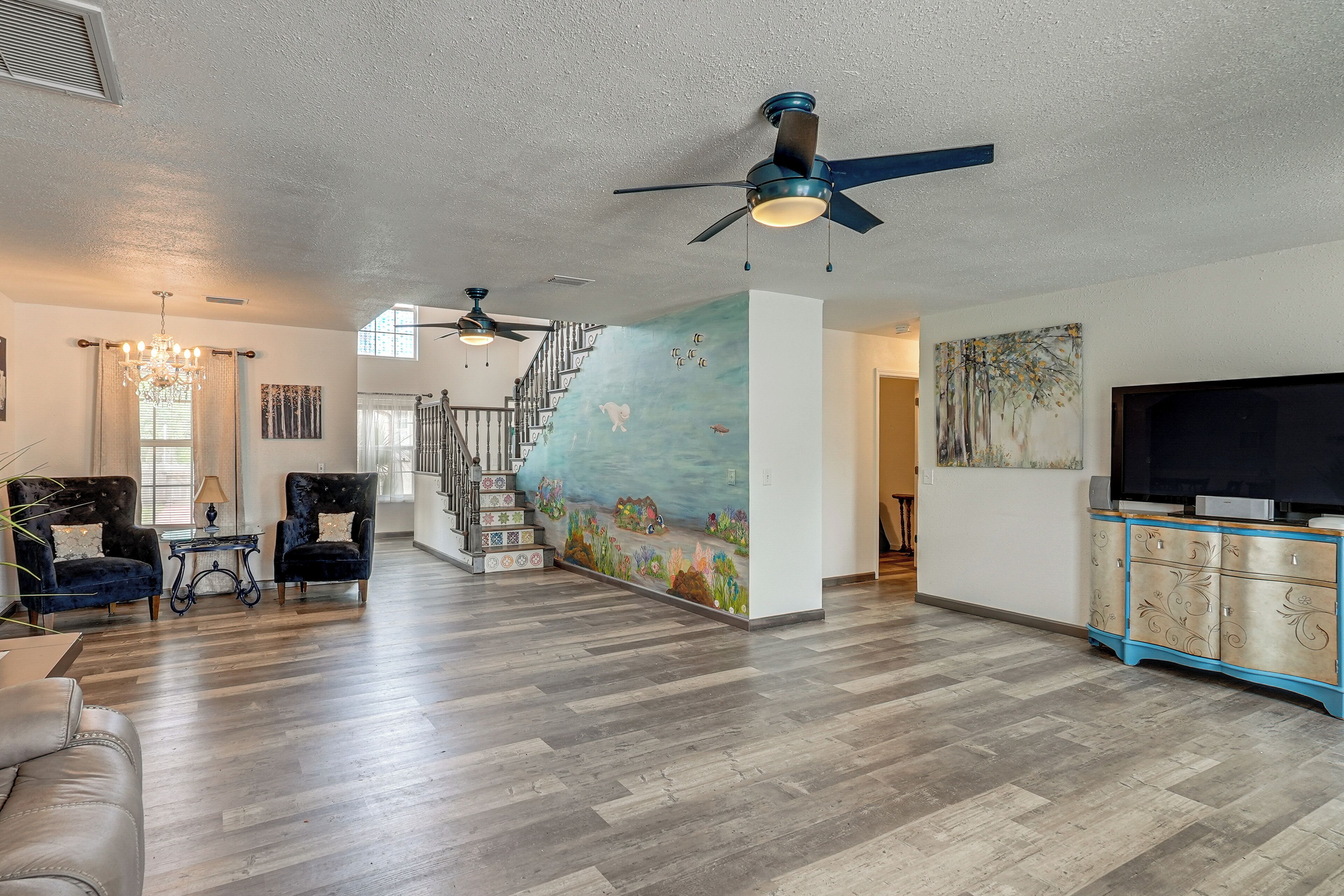 A spacious living area with a staircase, a large TV, and a mural on the wall.