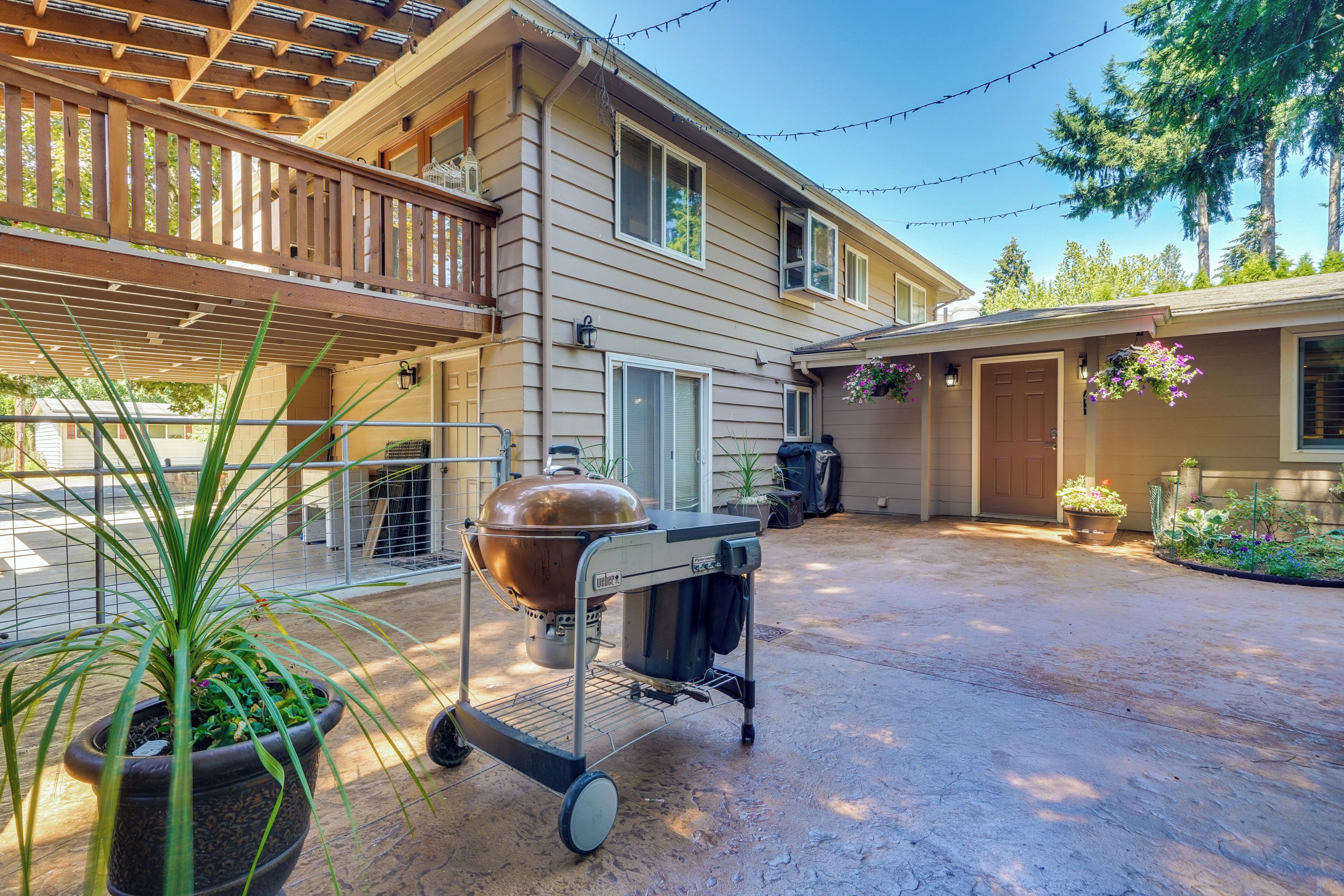 A covered patio area with a barbecue grill, potted plants, and a wooden deck.