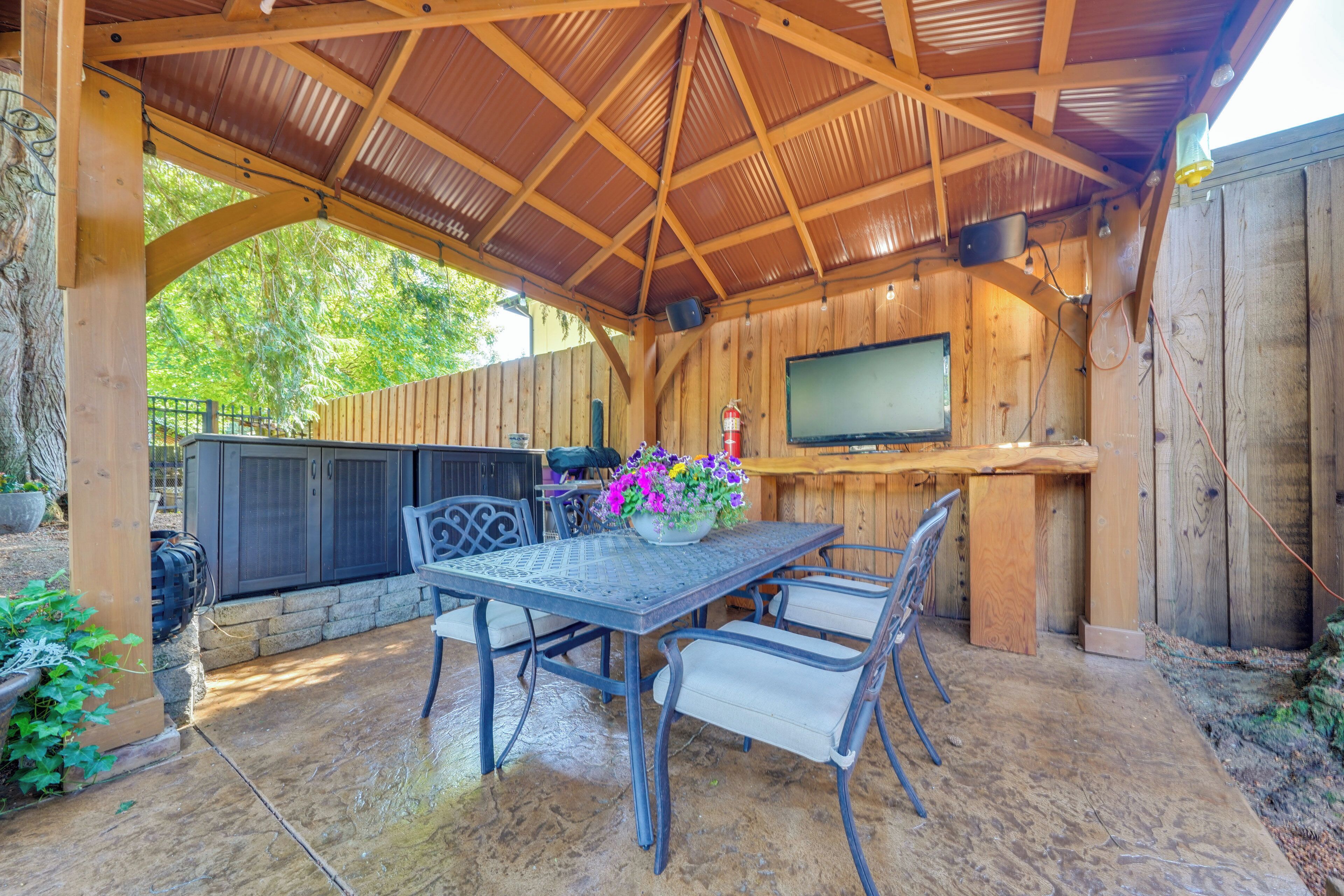 An outdoor patio with a covered seating area, a fire extinguisher, and a television mounted on a wooden wall.