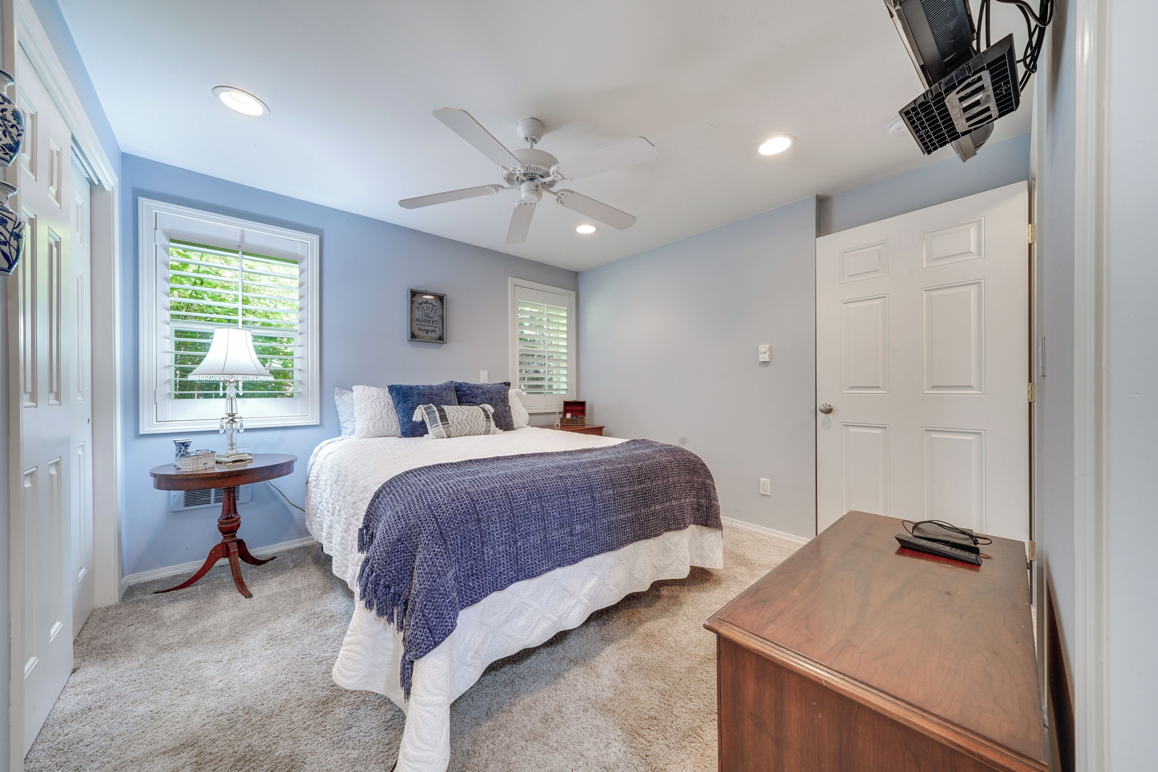 A bedroom with a bed, a ceiling fan, a desk, and a window with blinds.