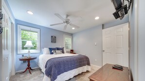 Un dormitorio con cama, ventilador de techo, escritorio y ventana con persianas.
