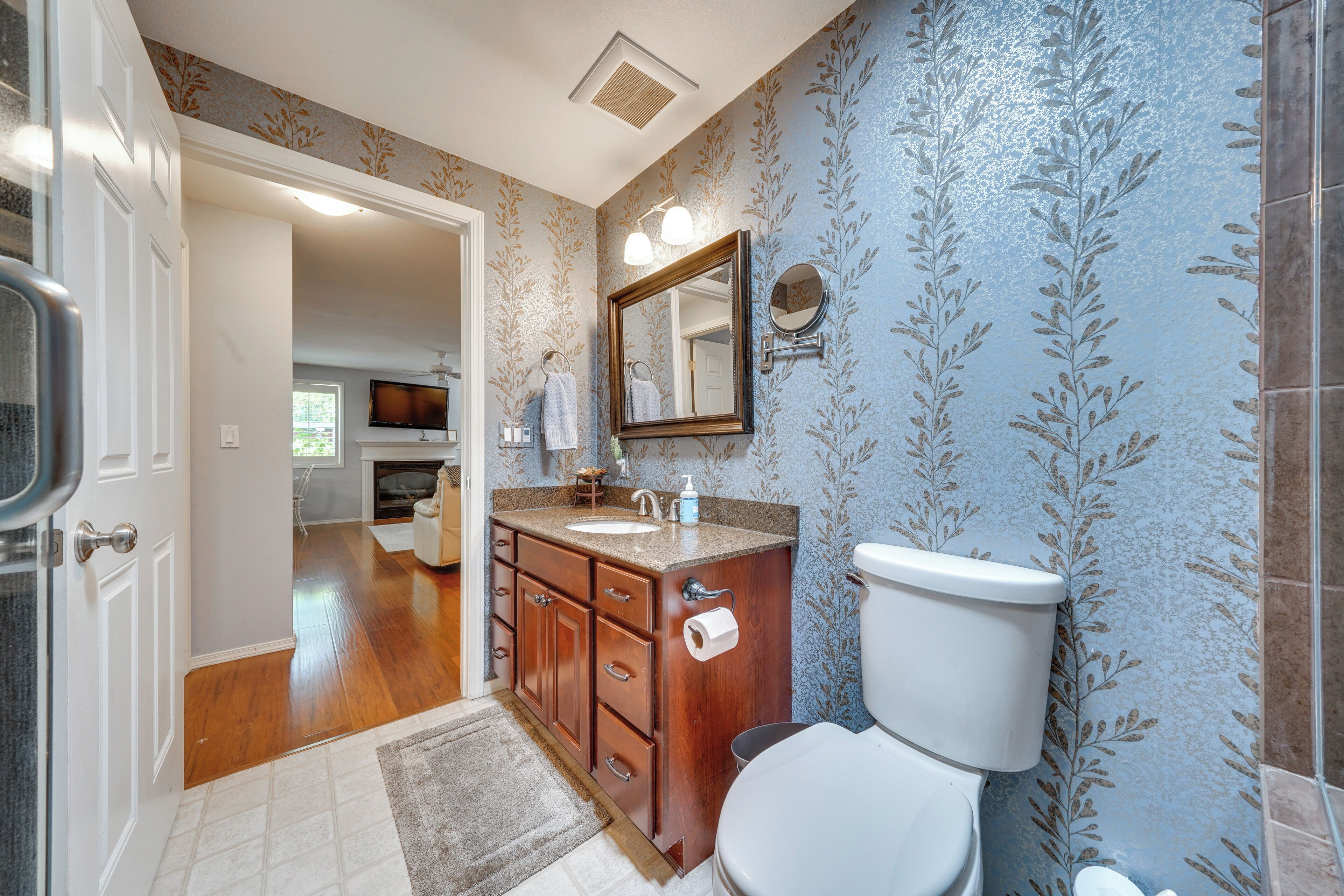 A bathroom with a wooden vanity, a toilet, a mirror, and a sink.