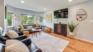 A living room with a sofa, a coffee table, a TV, a cabinet, and a large window. - Seatac Getaway! Fully Fenced w/ Workspace (SeaTac)
