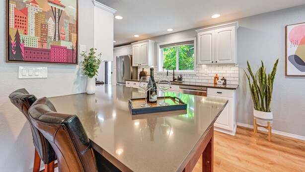 A modern kitchen with white cabinets, a large island, and a cityscape painting. - Seatac Getaway! Fully Fenced w/ Workspace (SeaTac)