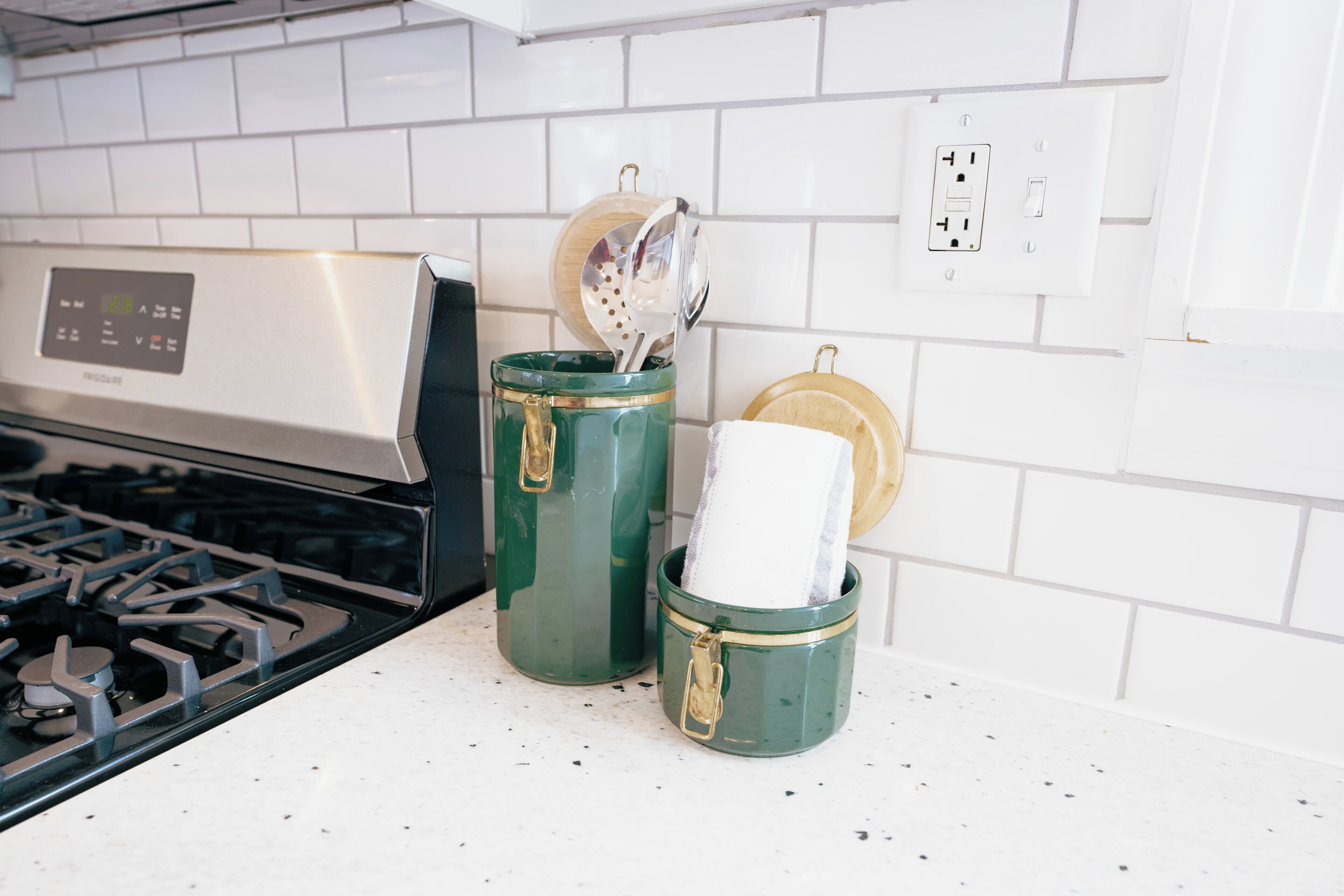 A kitchen with a stove, two green containers with lids, and a power outlet on the wall.