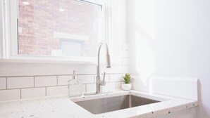 A kitchen with a stainless steel sink, white tiled backsplash, a window, and a small potted plant on the counter. - Walkable Oakley Neighborhood Home in Cincinnati! (Cincinnati)
