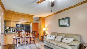 A kitchen with wooden cabinets, a microwave, and a refrigerator. There is a dining area with a table and chairs. A sofa is placed in the living area. - Explore Baton Rouge! Cozy Retreat w/ Private Yard (Baton Rouge)