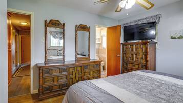 A bedroom with a bed, dresser, TV, and ceiling fan.
