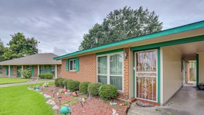 A two-story brick house with a green roof, a front porch, and a well-maintained garden. - Explore Baton Rouge! Cozy Retreat w/ Private Yard (Baton Rouge)