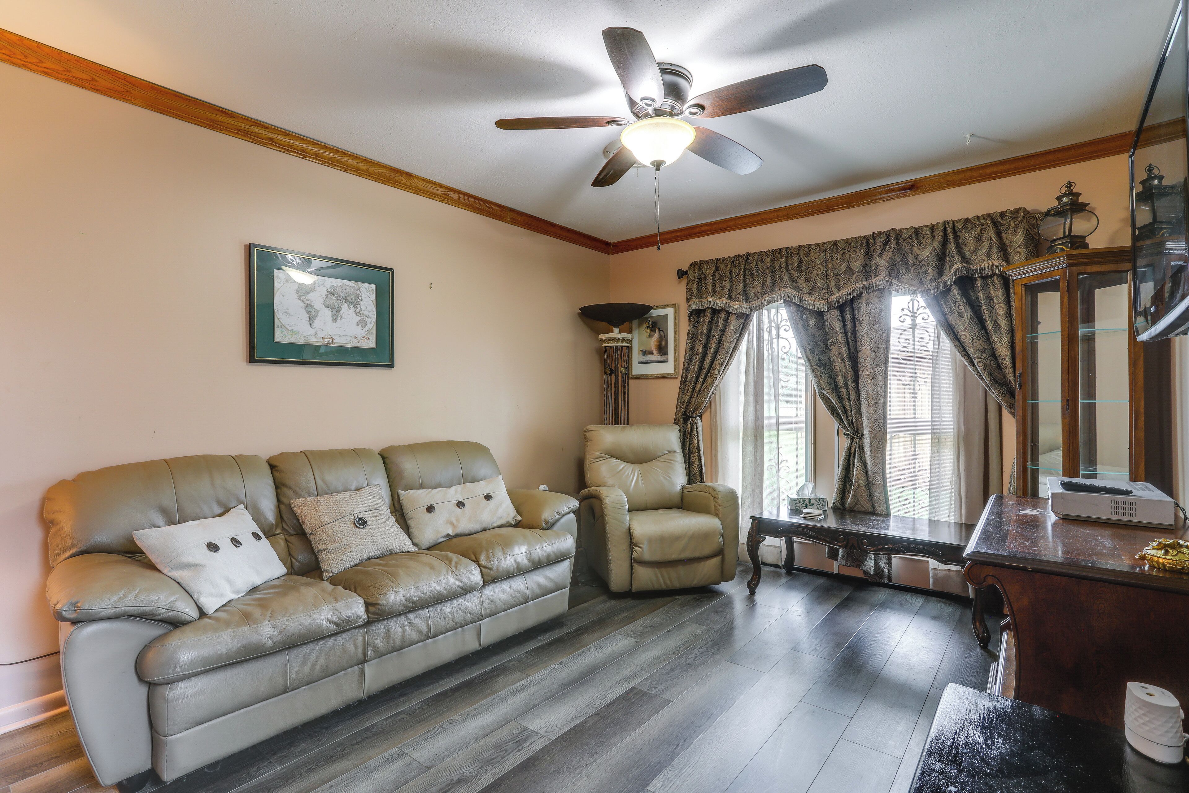 A living room with a leather sofa, a recliner, a ceiling fan, a world map, and a window with curtains.