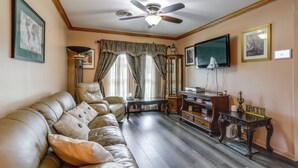 A living room with a sofa, a ceiling fan, a television, and a table with a lamp. - Explore Baton Rouge! Cozy Retreat w/ Private Yard (Baton Rouge)