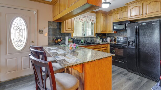 A kitchen with wooden cabinets, a granite countertop, a black refrigerator, and a dining area with chairs and a table. - Explore Baton Rouge! Cozy Retreat w/ Private Yard (Baton Rouge)