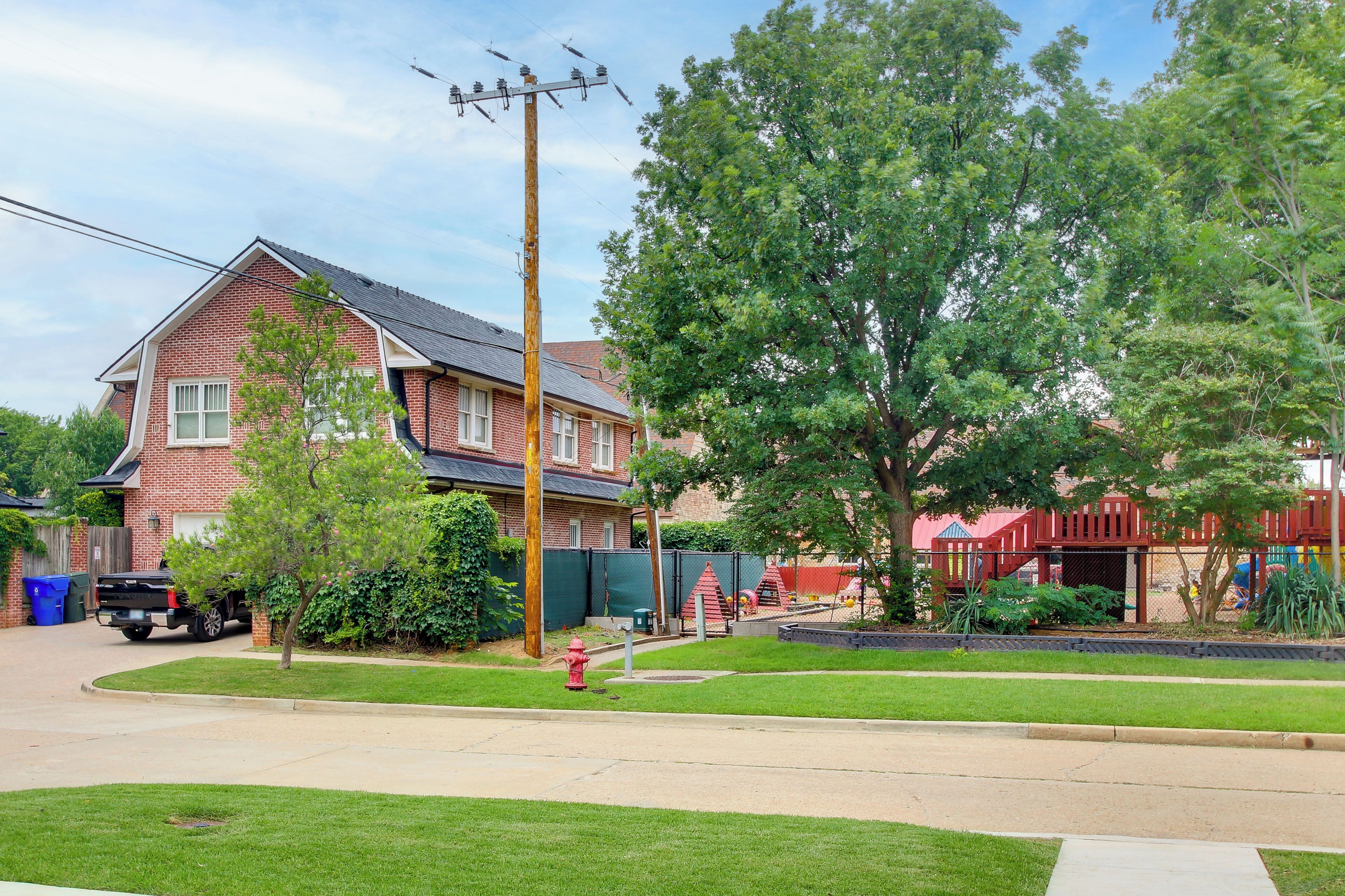 A residential area with a brick house, a driveway, a red fire hydrant, and a playground.