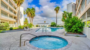 Una piscina con escalera de metal, rodeada de palmeras y un edificio con balcones.