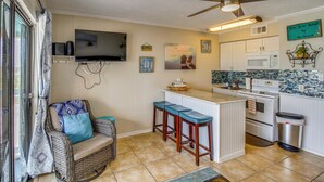 Una cocina con televisión de pantalla plana, taburetes de bar, ventilador de techo y salpicadero de azulejos.