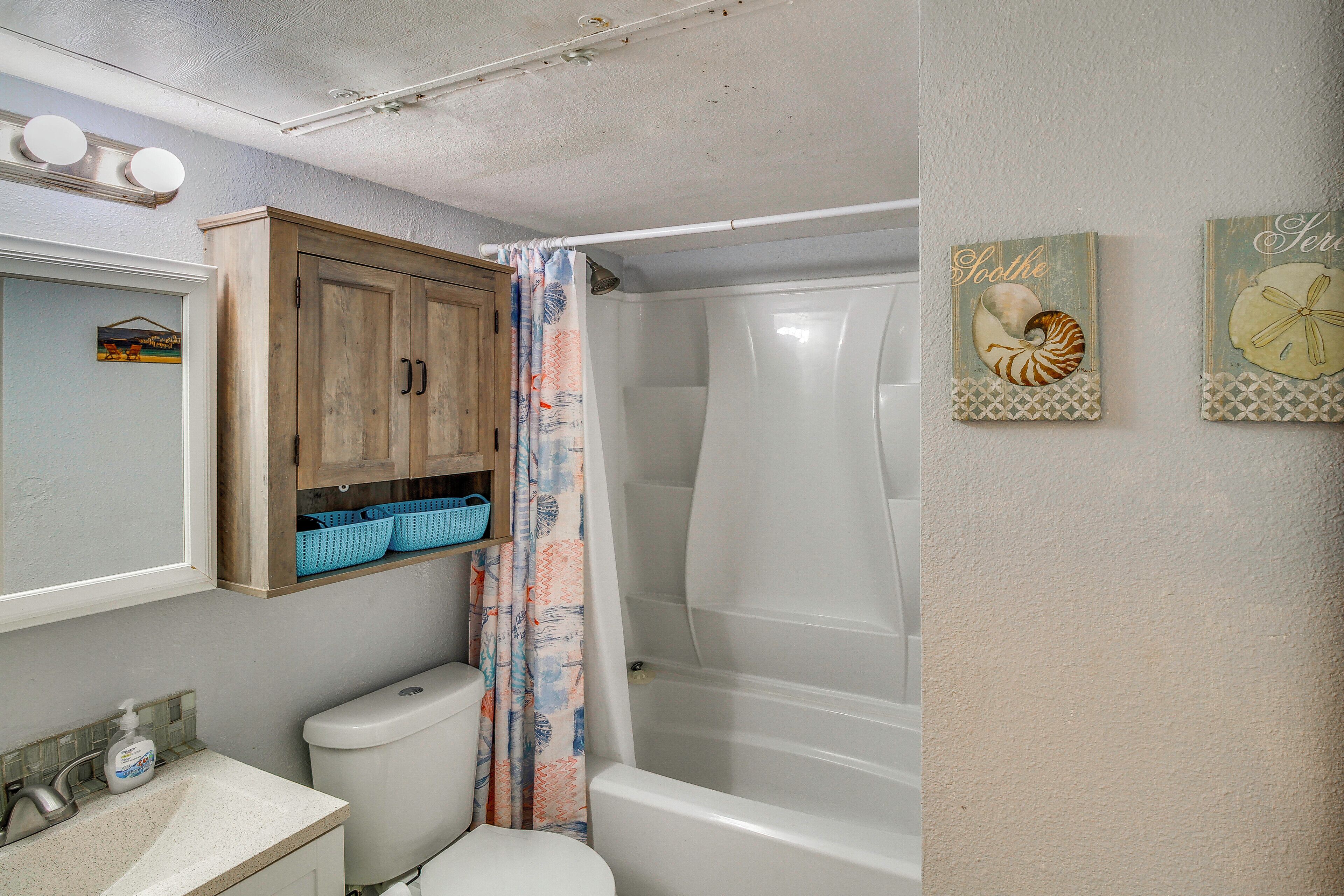 A bathroom with a toilet, sink, wooden cabinet, shower curtain, and two wall-mounted artwork pieces.