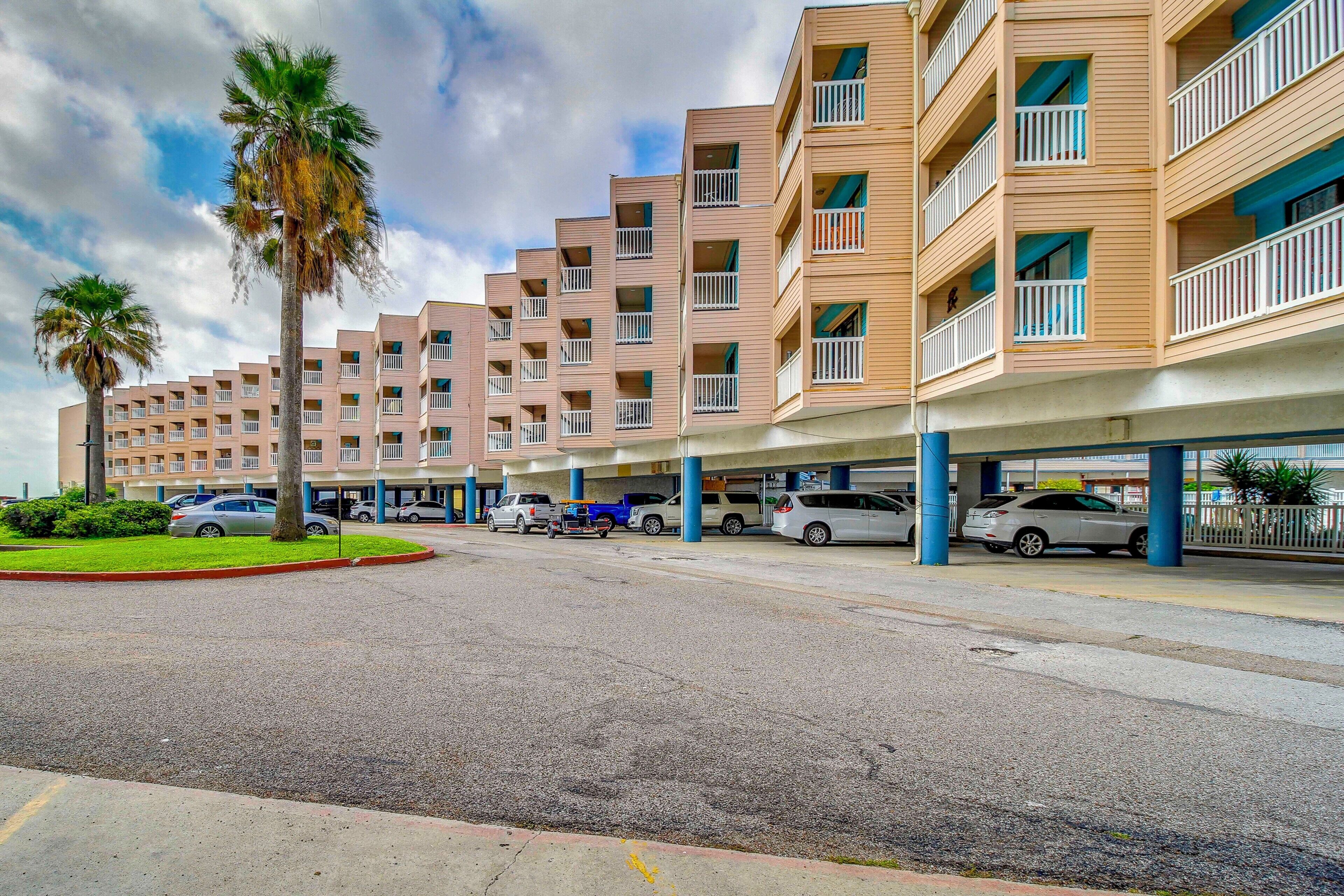 A multi-story hotel with balconies, a parking area, and palm trees.