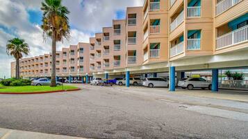A multi-story hotel with balconies, a parking area, and palm trees.
