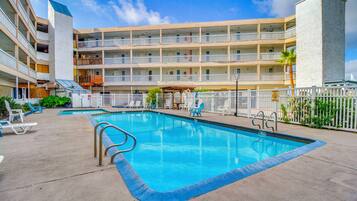 A multi-story hotel with a swimming pool, outdoor seating, and a fenced area.