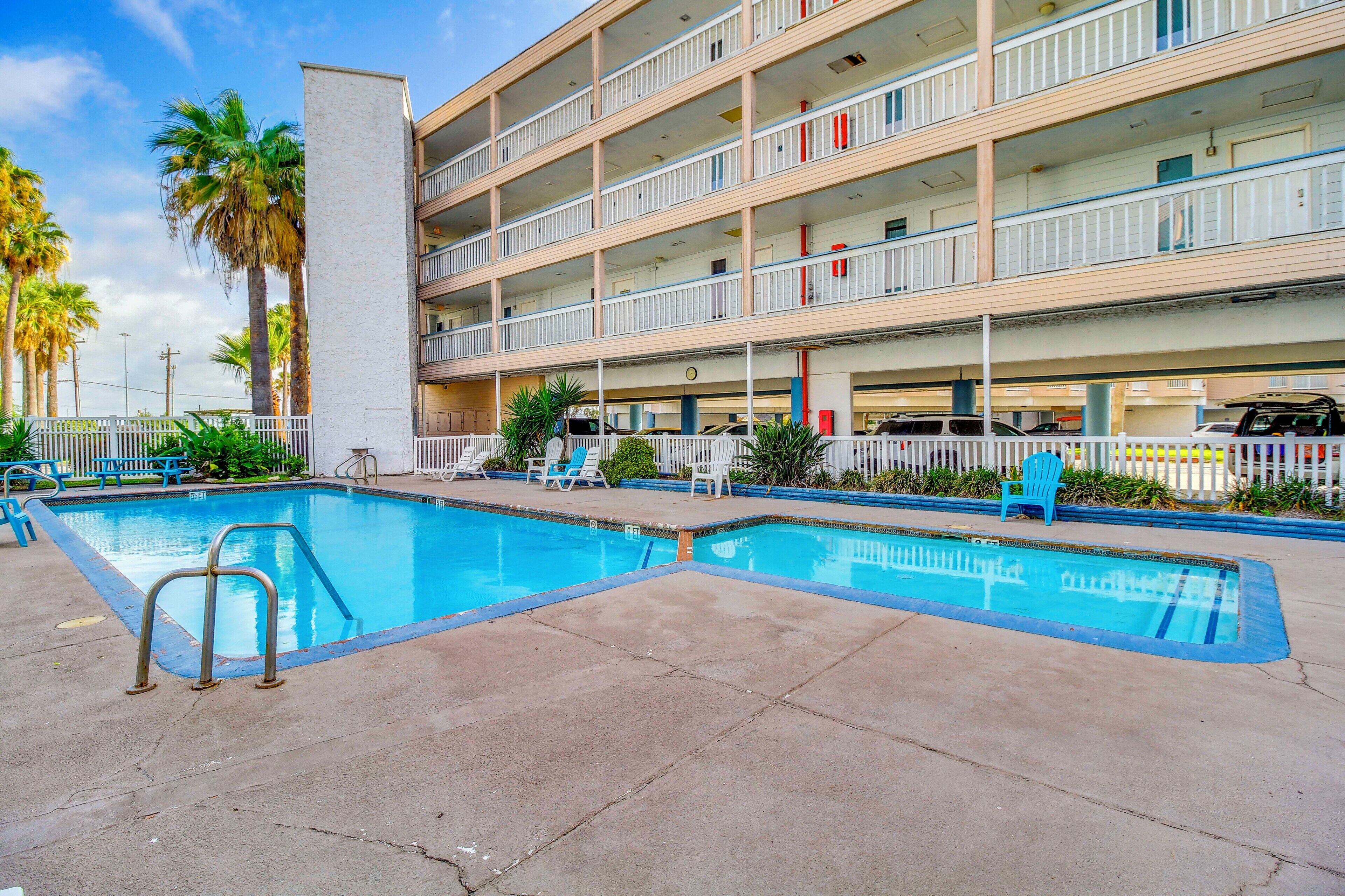 A hotel with a pool, multiple balconies, and a fenced area with lounge chairs.