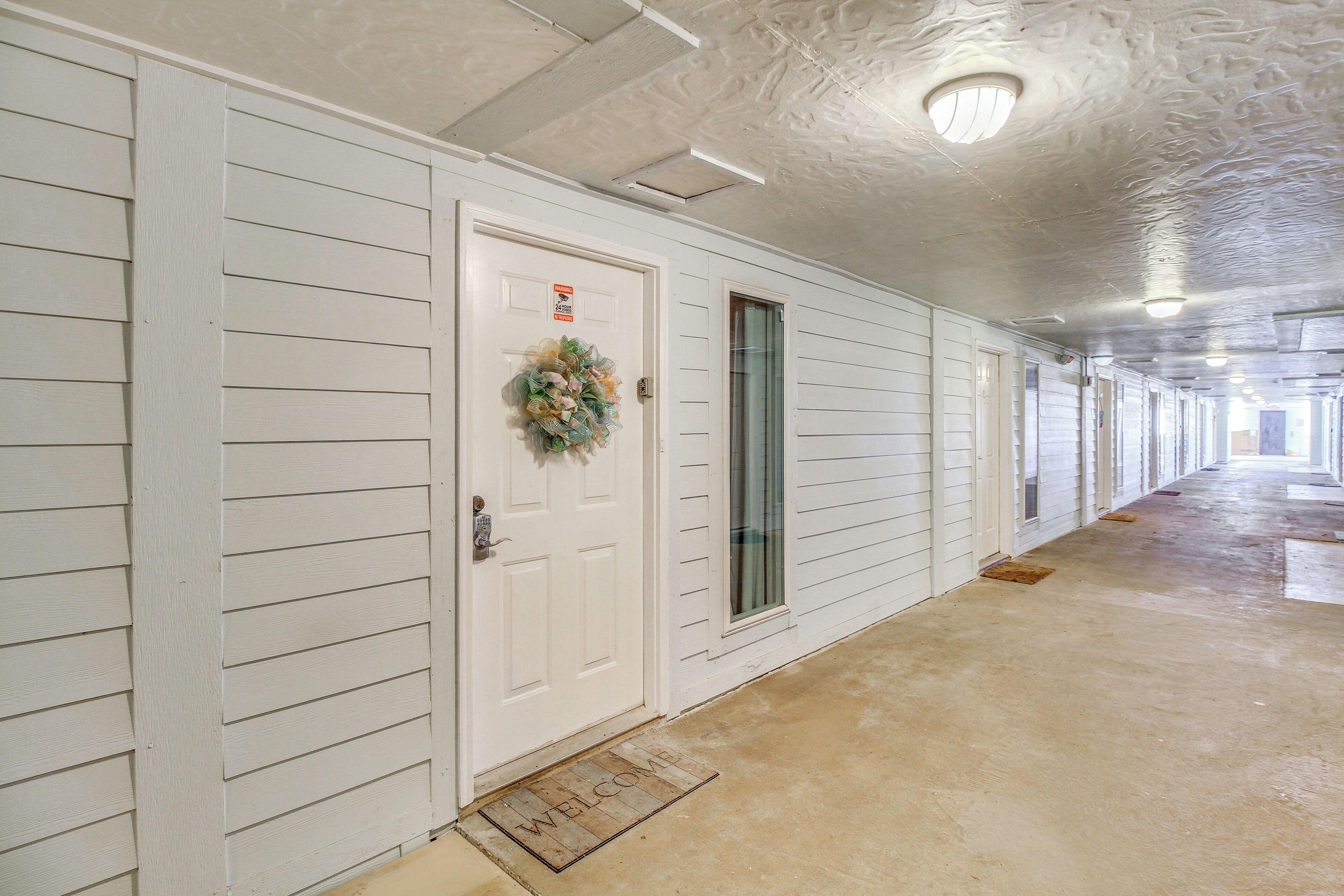 A hallway with a white door, a welcome mat, and a light fixture on the ceiling.
