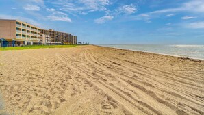 Un hotel frente a la playa con una extensa playa de arena, cielo azul despejado y mar tranquilo.