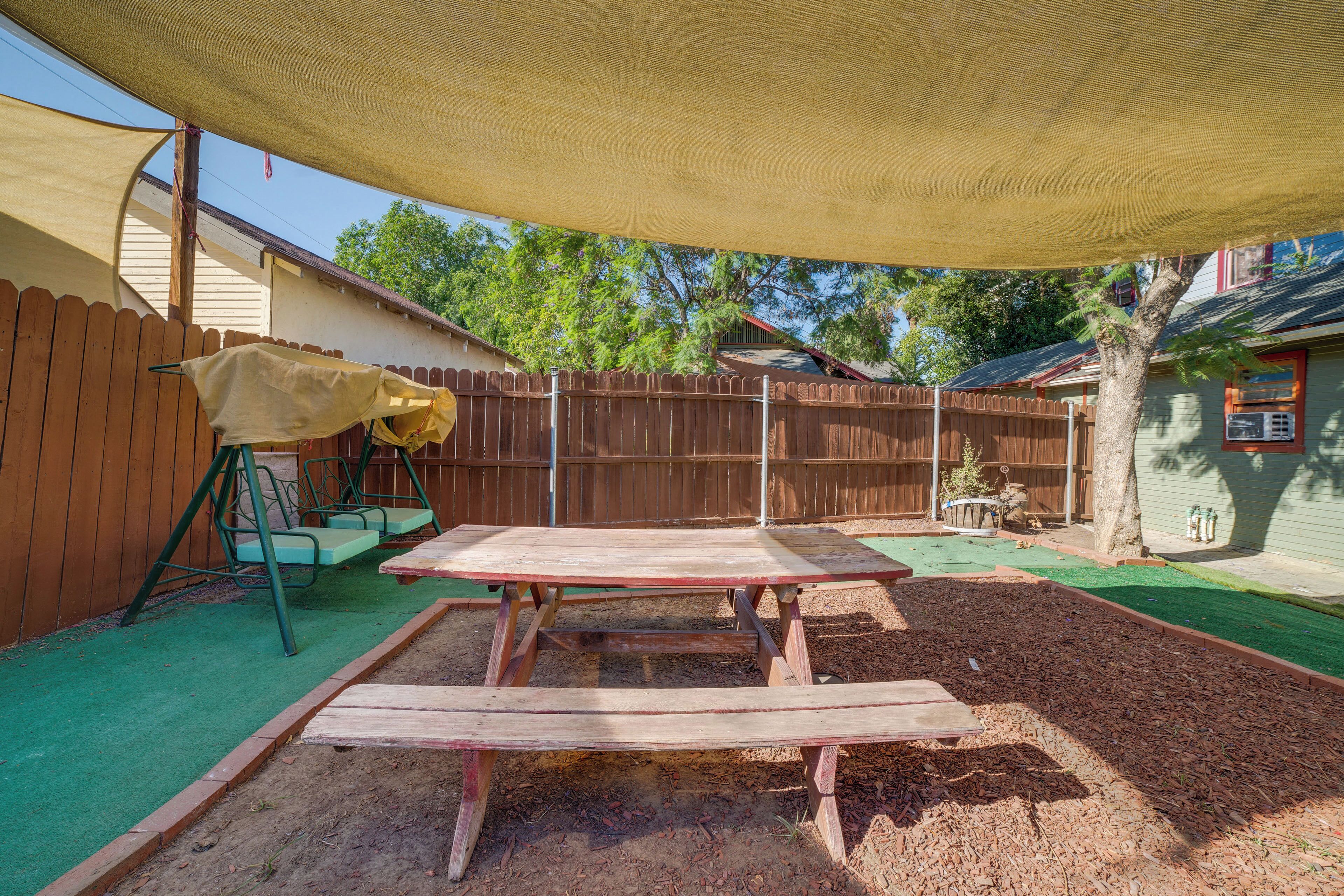 A backyard with a wooden table, a swing set, and a shaded area.
