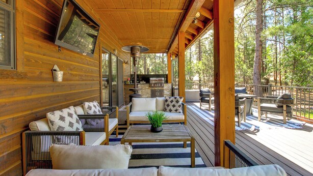 A wooden deck with outdoor seating, a TV mounted on the wall, and a view of the surrounding forest. - Outdoor Oasis w/ Fire Pit & Grill! Torreon Escape (Show Low)
