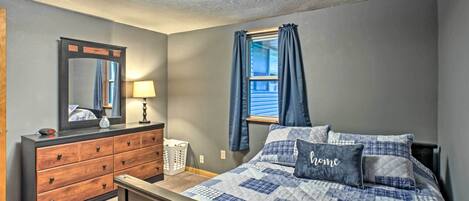 A bedroom with a bed, dresser, mirror, lamp, and window with curtains.