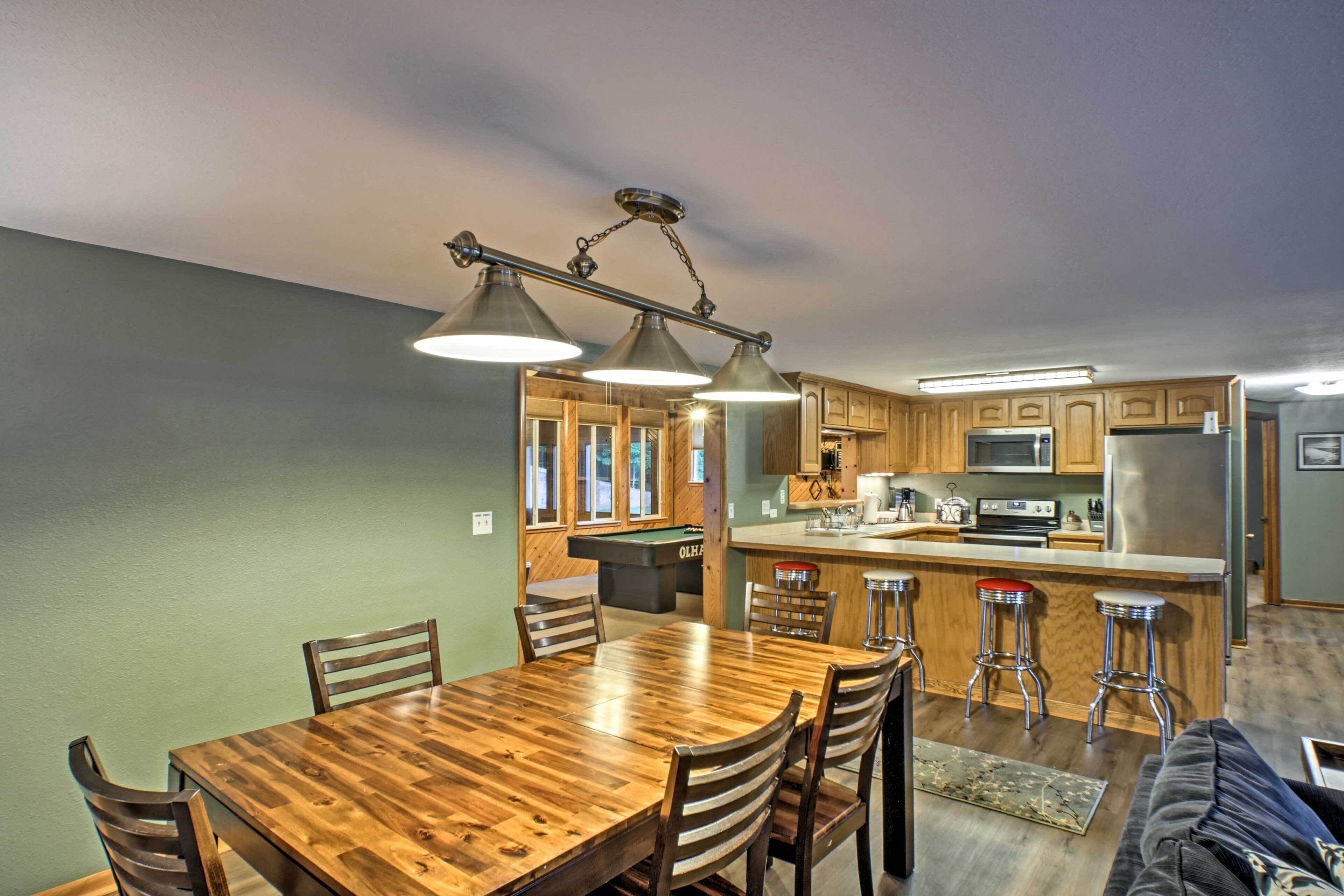 A modern kitchen with wooden cabinets, a central island with stools, and pendant lighting.