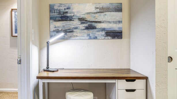 A corner desk with a white drawer unit, a desk lamp, and a painting on the wall. - Work, Play & Explore w/ Ease! Dtwn Meridian Apt (Meridian)