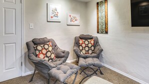 A room with two grey armchairs with patterned cushions, a white door, and a wall with two framed floral artworks. - Work, Play & Explore w/ Ease! Dtwn Meridian Apt (Meridian)
